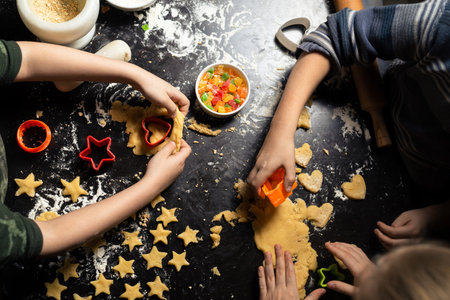 Children prepare star-shaped birthday cookies on a dark kitchen table. Family joint activity in the kitchen at home. View from above.の写真素材