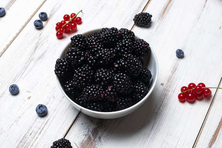 Fresh blackberries in a plate on a white wooden background.