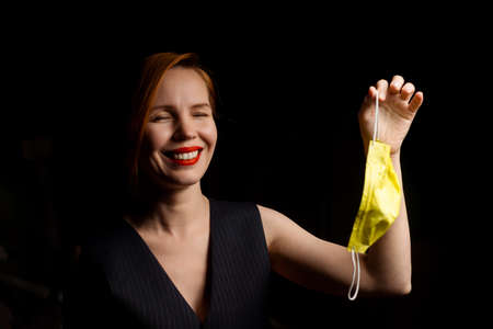 Freedom from the medical mask. Woman laughs contentedly holding a medical mask in her hand on a dark...