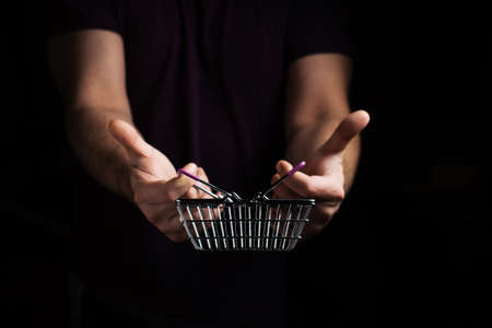 A man's hand holds an empty grocery basket on a dark background. Shopping concept.