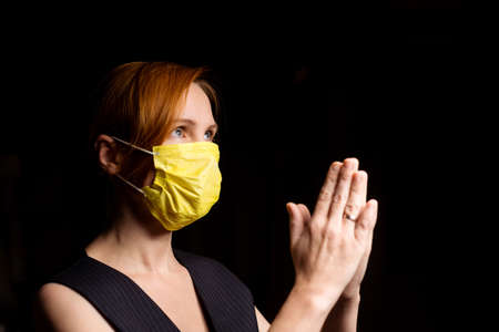 Woman prays in a medical mask on a black background.の写真素材