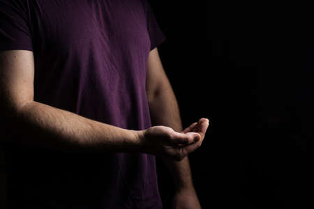 Empty male hand, palm up on a black background. Giving, asking concept.