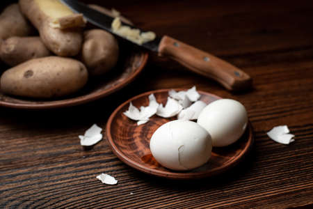 Peeling chicken eggs on a dark wooden background. In the background, out of focus, boiled unpeeled...