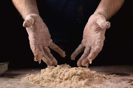 Cooking, kneading dough. Male hands mix the ingredients for the dough on the table against a dark...