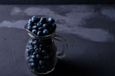 Glass jug with blueberries on a dark background. The benefits of berries, vegetarianism concept.の写真素材