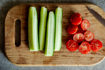 Sliced cherry tomatoes and cucumbers on a wooden board. Preparation for cooking salad. Vegetarian food.の写真素材