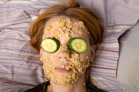 A woman makes a cosmetic mask at home from oatmeal on her face and cucumber. Anti-aging treatments, skin care concept.の写真素材