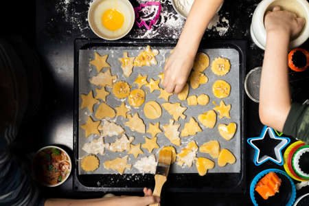 Children put cookies on a baking sheet. Cooking different forms of cookies for the holiday.の写真素材