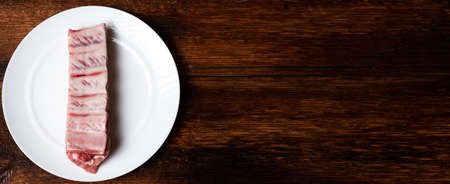 Fresh raw meat and pork ribs on a white plate on a wooden background. Banner, place for text.の写真素材