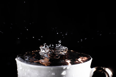 A drop of water falls into a cup on a black background. Splash on the water surface.