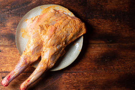 Raw lamb leg spread with spices, cooked for cooking on a plate on a wooden background.