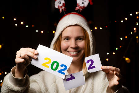 A woman smiles and changes the year 2021 to 2022 wearing a New Year's hat in the dark.