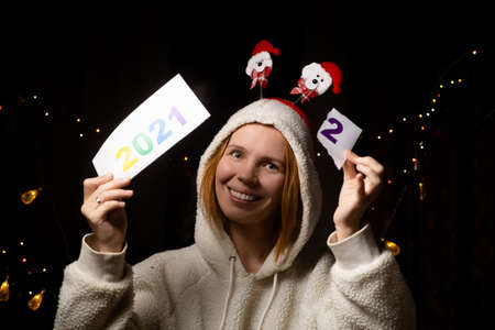 A woman smiles and changes the year 2021 to 2022 wearing a New Year's hat in the dark.
