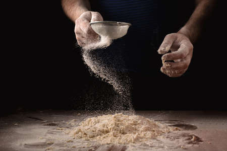 Cooking, kneading dough. Male hands sift flour onto the dough on a dark background.の写真素材
