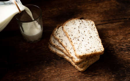 Pieces of bread with seeds and milk are poured into a glass. Dark wooden background. Morning breakfast. Healthy food.の写真素材