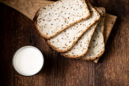 A full glass of milk. Bread in the background is blurred. Dark wooden background. Morning breakfast. Rustic styleの写真素材