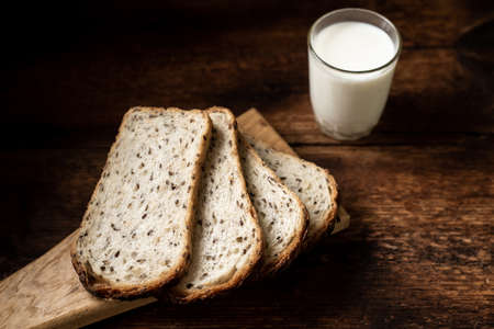 Pieces of bread with seeds and a glass of milk. Dark wooden background. Morning breakfast. Healthy food.の写真素材