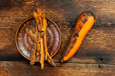 Peeling carrots. Dark wooden background. Half peeled carrots and dirty rind on a plate. Healthy food, vegetarianism. Top view.の写真素材