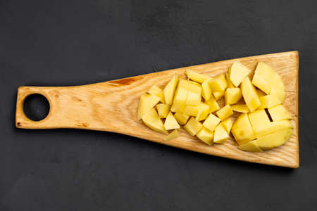 Sliced raw potatoes on a cutting wooden board. dark background. Preparation for cooking. Food background. Recipe.の写真素材