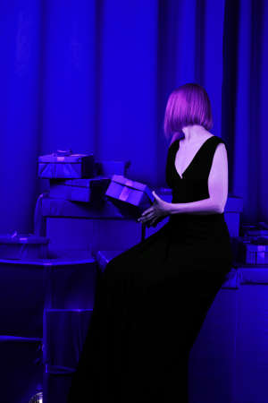 woman sits on a set of gifts. Middle-aged woman in a black dress. Blue background. Giving, receiving...