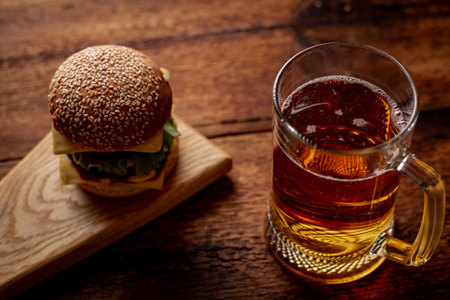 A glass of beer and a hamburger. Wooden dark background. Snack, food for beer.