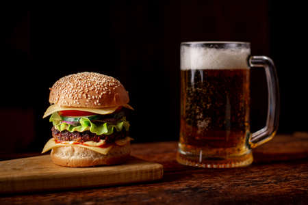 Hamburger on a wooden board and a glass of beer on the background. Snack for beer. dark background.