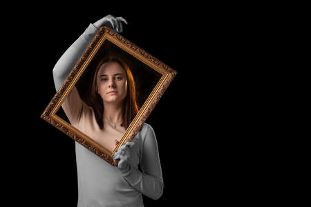Get out of the comfort zone, beyond the psychological framework concept. A young woman holds a picture frame in her hands on a dark background.の写真素材