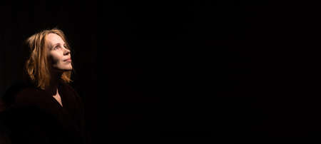 An attractive middle-aged woman looks up against a dark background. A woman of forty years old....