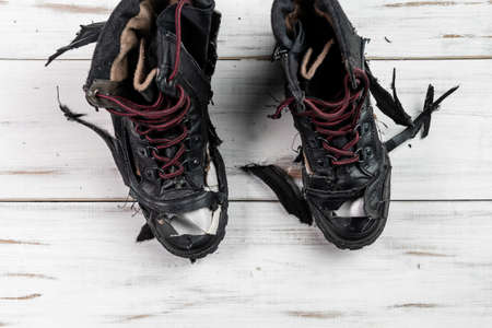 Torn worn boots. Light wooden background. Torn, broken shoes.