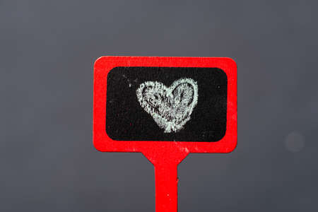 Red wooden plaque, surface painted with a heart. Black background.