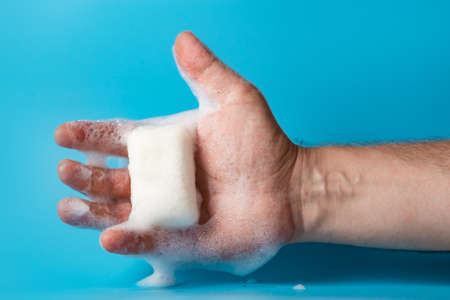 Global Handwashing Day, personal hygiene concept. A man's hand in foam holds soap on a blue background.の写真素材
