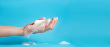 Global Handwashing Day. A bar of soap in a female hand on a blue background. Personal hygiene concept, hand washing. Banner, place for text.の写真素材