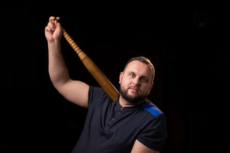 A young man is holding a wooden bat. Bouncer, security guard, bodyguard concept. A large man in a...