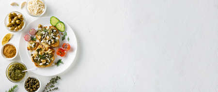 Vegetarian food concept. Cauliflower steak with spices, chimichurri sauce, almond flakes, olives, fried cherry tomatoes and capers on a white plate. white background. Banner, place for text.の写真素材