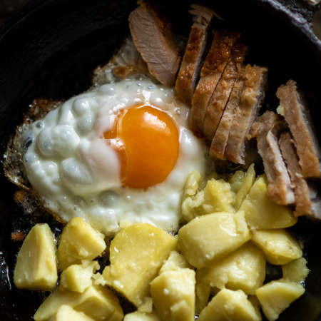 Fried eggs, potatoes and meat in a frying pan. breakfast preparation.の写真素材