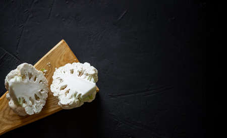 Half cut cauliflower on a dark background. Cooking cauliflower steak. Vegetarian food, diet concept.