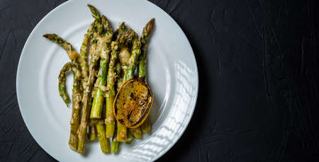 Asparagus baked with cheese and lemon on a white plate. dark background. Vegetarian food. Health food.の写真素材