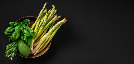 Various green vegetables on a dark background. Asparagus, spinach, avocado. Vegetarian food concept. Banner. Place for text. top view.の写真素材