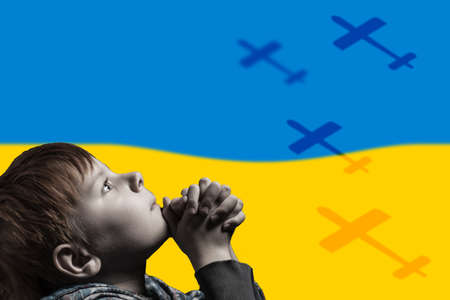 A child prays against the background of the Ukrainian flag. Russian aggression. flying planes.の写真素材