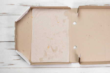 Empty open pizza box. White wooden background. Eaten pizza. Top view.