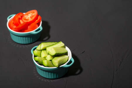 Sliced cucumbers and tomatoes in cups on a dark background. Salad ingredients. minimalism. Raw vegetables, vegetarianism.の写真素材
