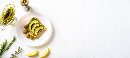 toast with avocado, olives and chimichurri sauce on a white plate. Healthy vegetarian food. white background. Banner. Place for text.の写真素材