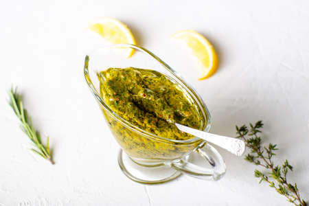 Chimichurri sauce in a gravy bowl on a white background. Argentinean vegetarian sauce made from...
