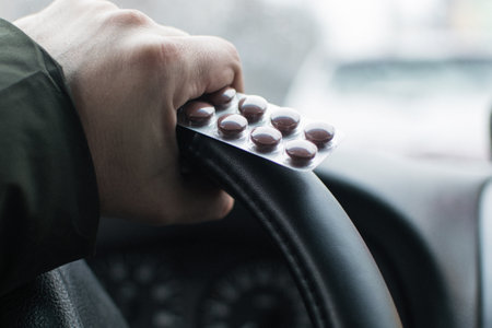 Medical pills and car driving. Male hand holds blister with pills on the steering wheel.