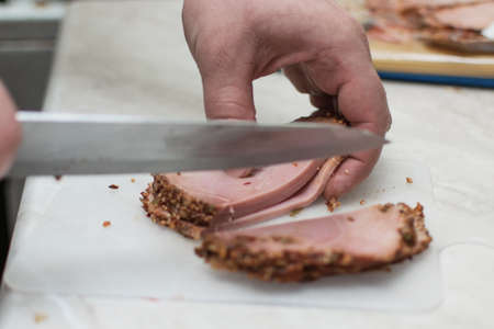 Male hands cut ham, prepared meat on a cutting board.の写真素材