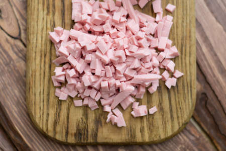 Chopped boiled sausage on a wooden board.