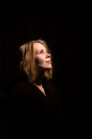 An attractive middle-aged woman looks up against a dark background. A woman of forty years old....