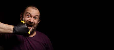 A man rips off a medical mask. Screaming man. Black background. Protest against quarantine concept....