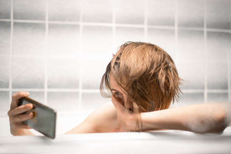 Sensual middle-aged woman takes a bath and communicates on a mobile phone by video communication....