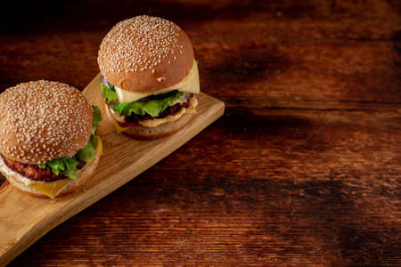 Two hamburgers on a wooden background. Big and small cheeseburger. Hamburger day.の写真素材